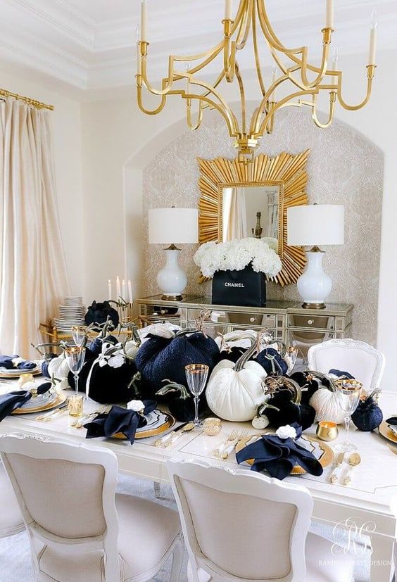 a glam Thanksgiving tablescape with large black and white velvet pumpkins, gold chargers, cutlery and candleholders plus black napkins