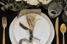 09 a gorgeous glam Thanksgiving table setting with a black uncovered table, white plates, gold cutlery, white florals and greenery and wheat