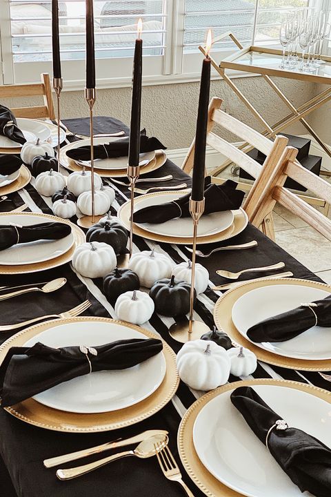 a lovely and refined Thanksgiving tablescape with a striped runner and black napkins, black and white pumpkins, tall and thin black candles and gold cutlery