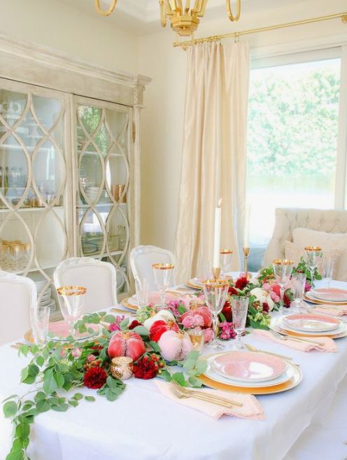 a lovely glam Thanksgiving tablescape with pink, blush, red velvet pumpkins, greenery, blush and white plates, gold cutlery and glasses with gold rims