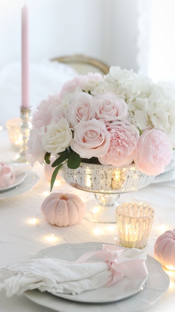 a refined and glam Thanksgiving tablescape with chic plates, neutral linens, blush pumpkins, blush and white florals and some lights and candles