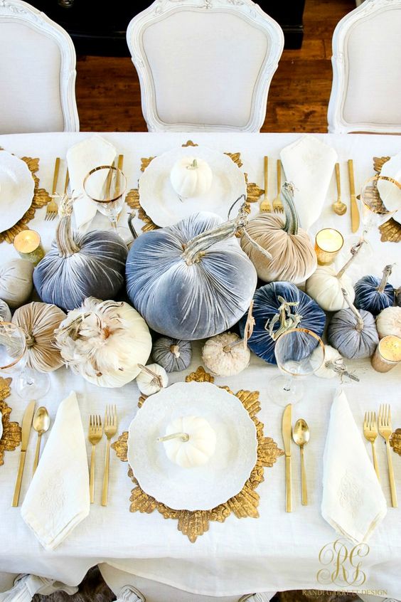 a sophisticated glam Thanksgiving tablescape with neutral, ligth blue and navy velvet pumpkins, gold chargers, cutlery and candles around