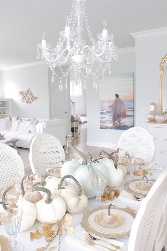 a super chic white and gold Thanksgiving tablescape with lots of fabric pumpkins, gold chargers and cutlery, gilded leaves