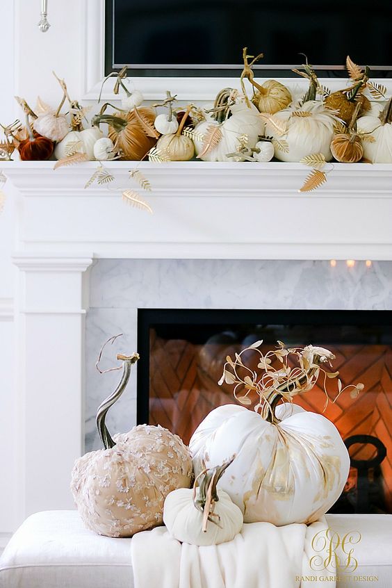a glam Thanksgiving mantel with white, rust and burgundy velvet pumpkins, gilded leaves and pretty fabric pumpkins in front of it