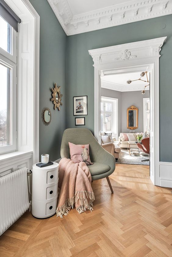 a beautiful Parisian-inspired space with green walls, beautiful ornated crown moldings and a parquet floor plus adorable mid-century modern furniture