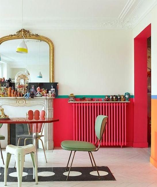 a bold vintage-inspired interior with red touches including a radiator, green stools and chairs, a faux fireplace and an oversized mirror