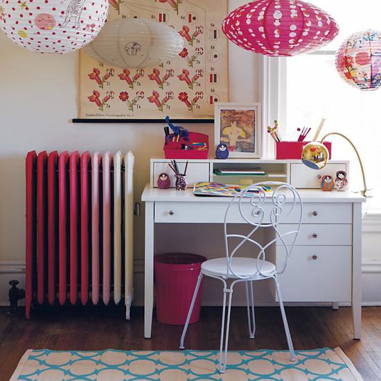 a bright space with an ombre pink radiator, a white desk and a chair, paper pendant lamps and bold artworks plus a bright rug