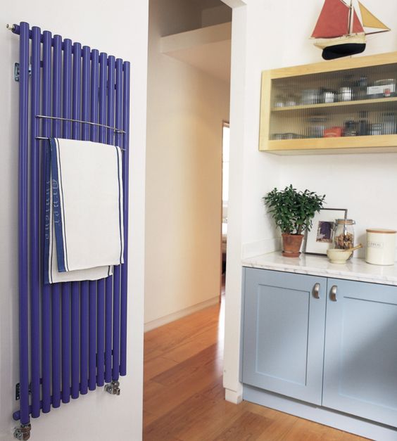 a catchy kitchen with pale blue and yellow cabinets, white stone countertops and a cobalt blue radiator on the wall