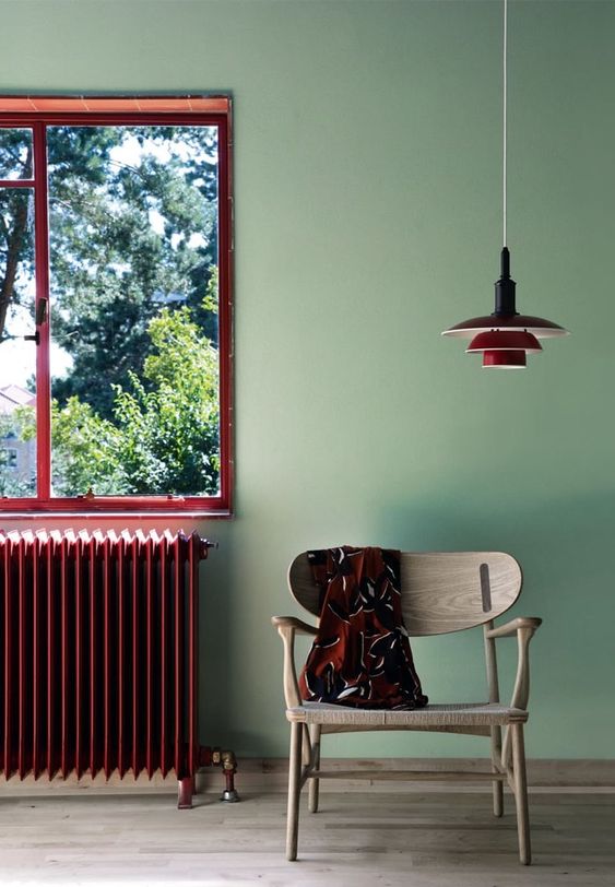 a catchy space with light green walls, a neutral stained floor, a burgundy window frame, a radiator and a pendant lamp that match