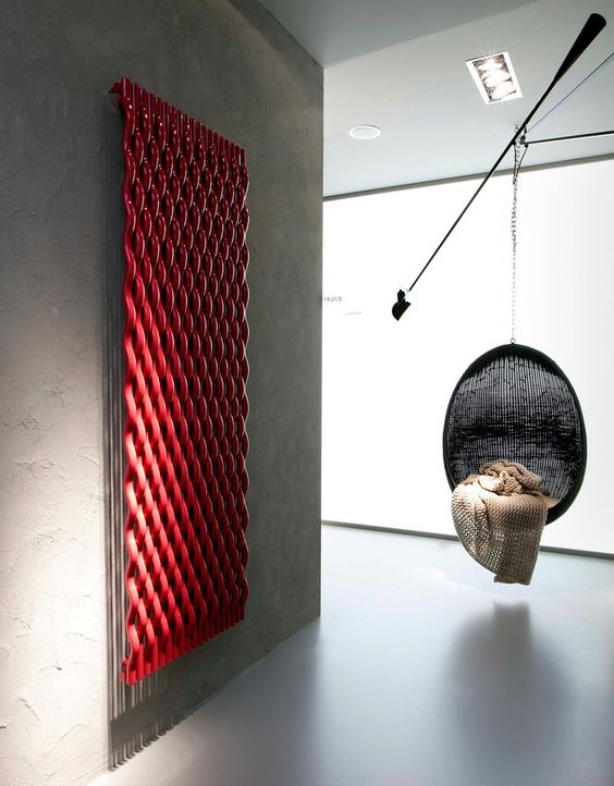 a contemporary space all done of concrete, with a black suspended chair and a red woven radiator on the wall is a pretty solution