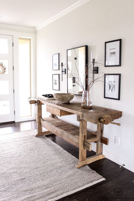 a delicate and airy greige entryway with a mini gallery wall with black frames, a stained vintage table, a neutral rug and lots of natural light