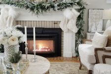 a fab winter wonderland Christmas space with faux fur stockings, an evergreen garland, mini trees on the mantel, neutral pillows and furniture