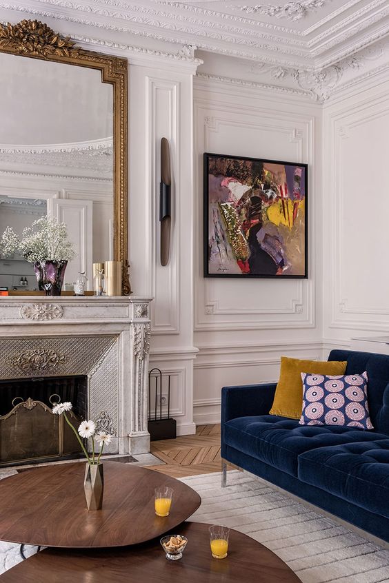 a fantastic Parisian living room with layered ornated molding, with a refined marble fireplace and a large mirror over it, with a navy velvet sofa