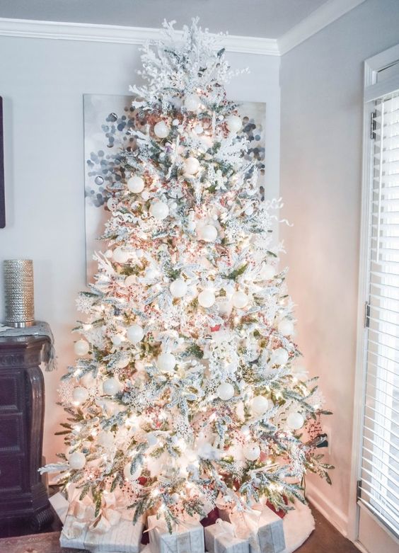 a flocked winter wonderland Christmas tree with white and silver ornaments, lights, red berries and greenery branches