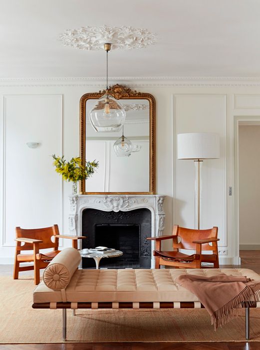 a gorgeous Parisian chic living room with ornated crown modling and a ceiling medallion, with a non-working fireplace, a chic couch and leather chairs