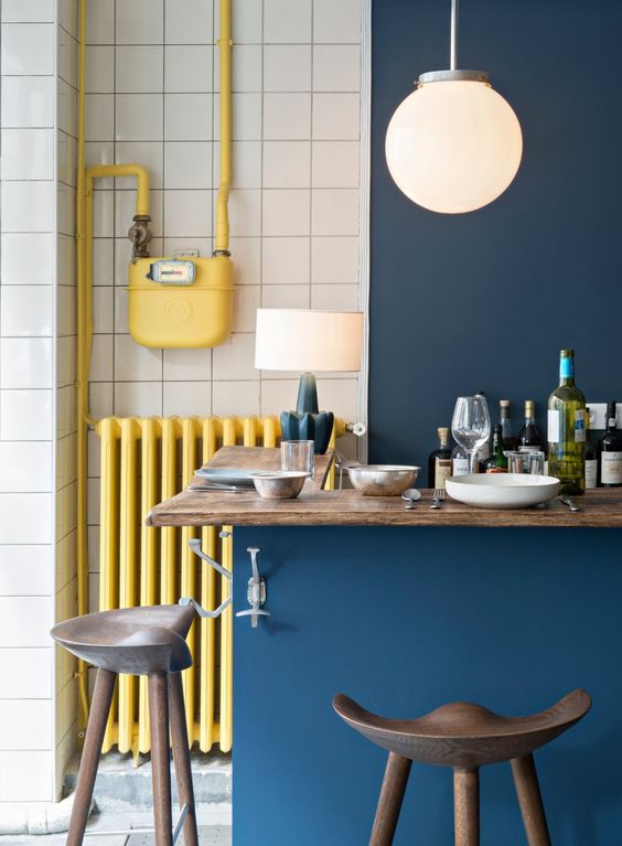 a lovely Parisian cafe chic kitchen in navy and white, with a kitchen island and butcherblock countertops and a yellow radiator and tubes
