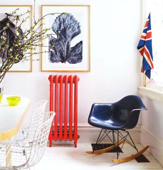 a lovely interior in neutrals with a bold red radiator, a navy chair and a pretty gallery wall is a chic space to be