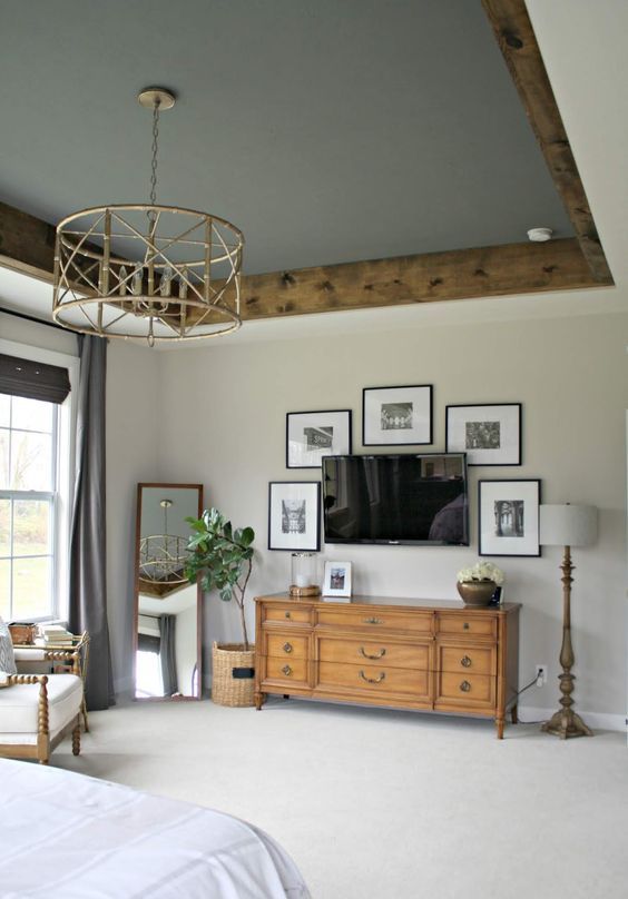 a modern farmhouse bedroom featuring a grey ceiling with stained rustic crown molding, a catchy chandelier, a mini gallery wall and vintage and modern furniture