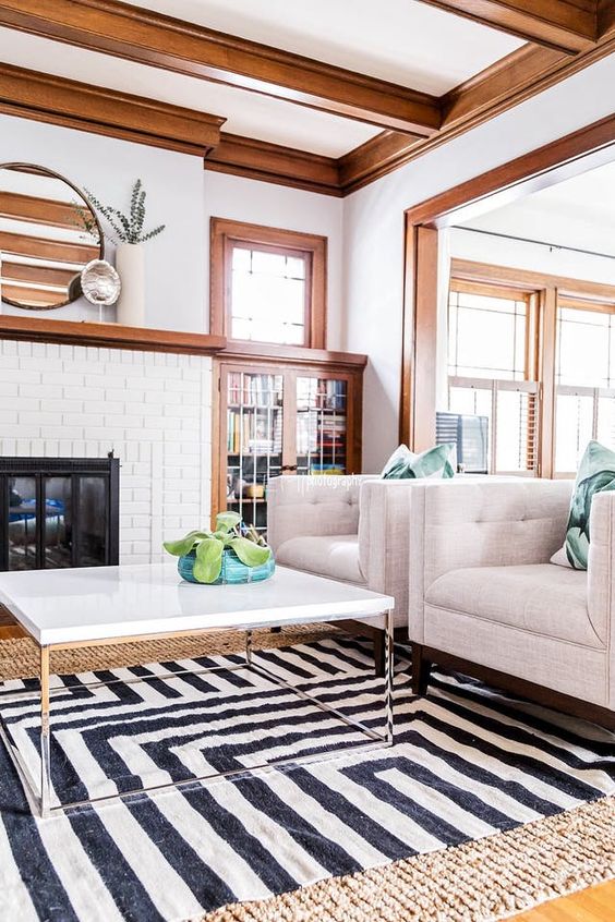 a modern farmhouse living room featuring rich-stained crown molding that frames the ceiling, the windows and the fireplace and matching wooden beams