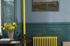 a moody vintage-inspired space with blue walls and dark green wainscoting, a neon yellow radiator and a tube, bold blooms