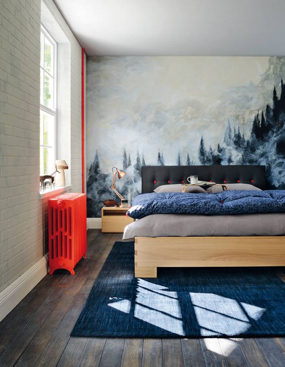 a pretty and welcoming bedroom with an artwork that takes a whole wall, modern furniture, a hot red radiator and a navy rug