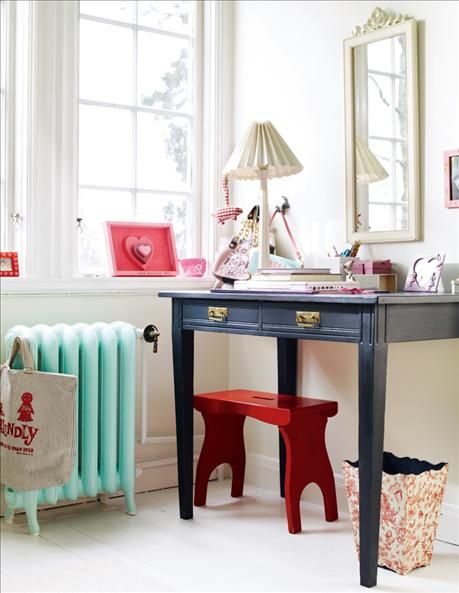 a pretty makeup nook by the window with a mint radiator, a black vanity and a red stool, a vintage lamp and a mirror in a matching vintage frame