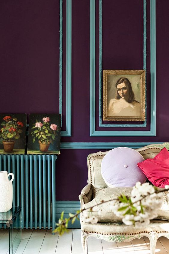 a refined space with deep purple walls with blue frames, a matching blue radiator, a refined loveseat and pastel pillows is wow