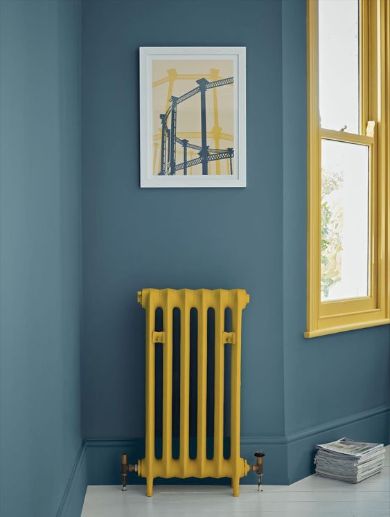 a slate blue space with a sunny yellow window frame and a matching radiator is a lovely and bold space with a contrasting touch