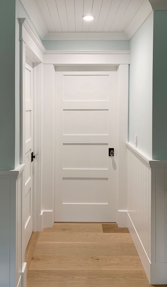 a small and lovely hallway accented with wainscoting and with crown molding that frames the doors and the ceiling for a neater look