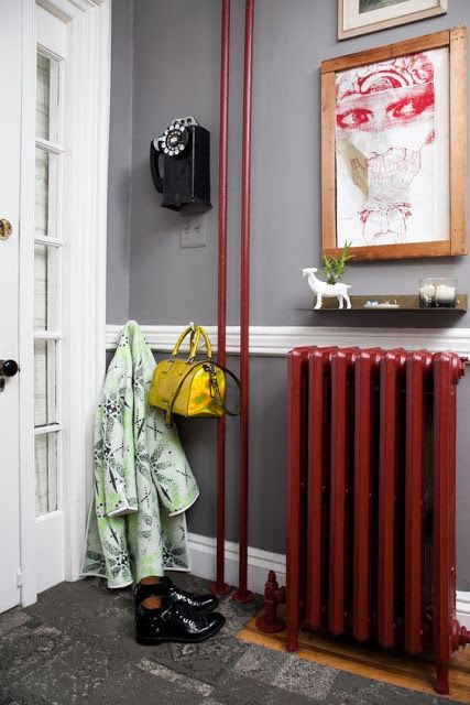 a small entryway with grey walls and grye rugs, a bold red radiator and tubes, a vintage phone and art that create a mood here