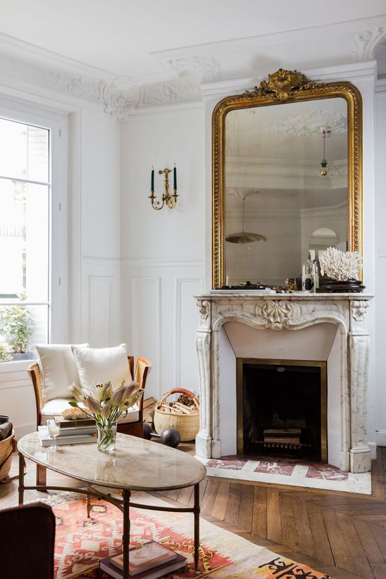 a sophisticated Parisian living room with ornated crown molding, with a refined fireplace and a gorgeous mirror ina  gilded frame, with neutral furniture