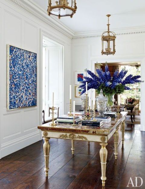 a statement and refined space with cool sculptural crown molding, a bold artwork, a refined table with lots of books and candleholders