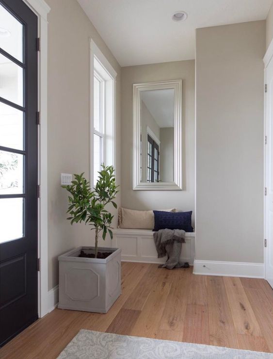 a stylish greige entryway with a built-in paneled bench, a planter with a tree and a tan and navy pillow is an elegant space
