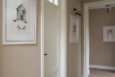 a stylish greige entryway with white touches, artworks and a vintage pendant lamp is a chic space with an elegant color scheme