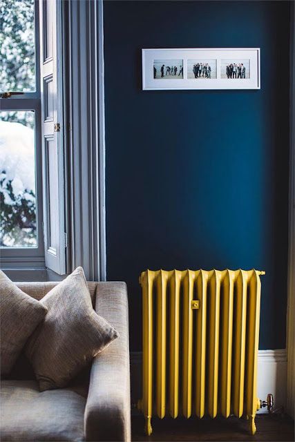 a stylish navy living room with white wainscoting, a grey sofa and a yellow radiator that adds color and a cheerful feel to the space