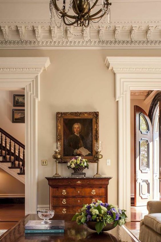 a super refined space with oversized ornated crown molding, a crystal chandelier, molding covering the doorways and vintage furniture