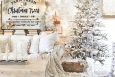 a winter wonderland Christmas living room with a flocked Christmas tree with lights, neutral furniture and linens, a Christmas sign with trees and lights