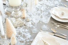 a winter wonderland Christmas table with pillar candles, bottle brush trees, faux snow and cool white porcelain and silver cutlery