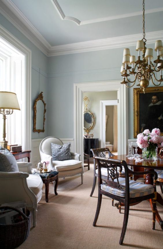 an elegant English country living room with white wainscoting and crown molding, with chic vintage furniture and a brass chandelier
