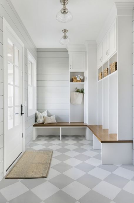 an elegant farmhouse greige mudroom with planked walls, white and stained storage furniture, a checked floor and lots of natural light