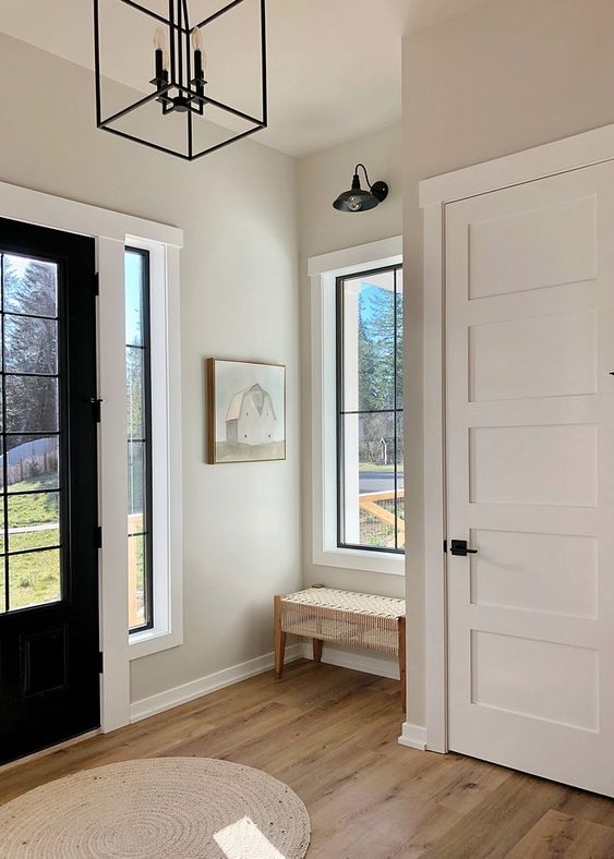an elegant modern entryway with crown molding framing the doorways, a black chandelier and a black door for an accent
