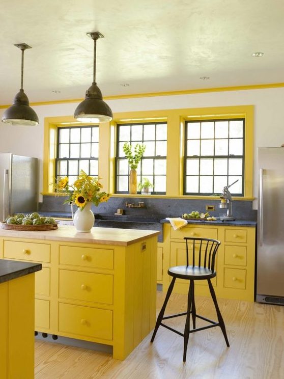 a bright farmhouse kitchen with bold yellow cabinets and window frames, grey stone countertops and a large sink
