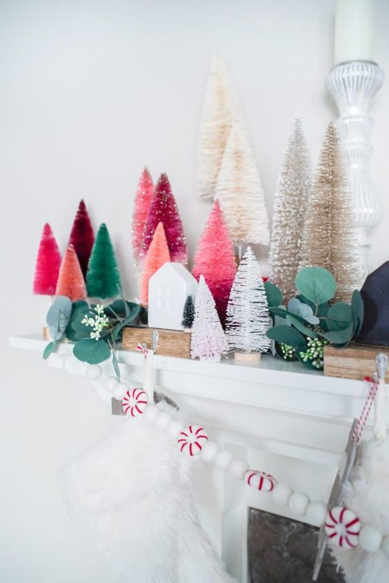 a chic Christmas mantel decorated with colorful bottle brush trees, fau greenery, a peppermint garland and mini houses