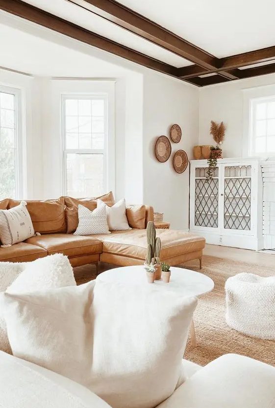 a welcoming boho living room with dark beams, an amber leather sofa, white furniture and decorative baskets on the wall