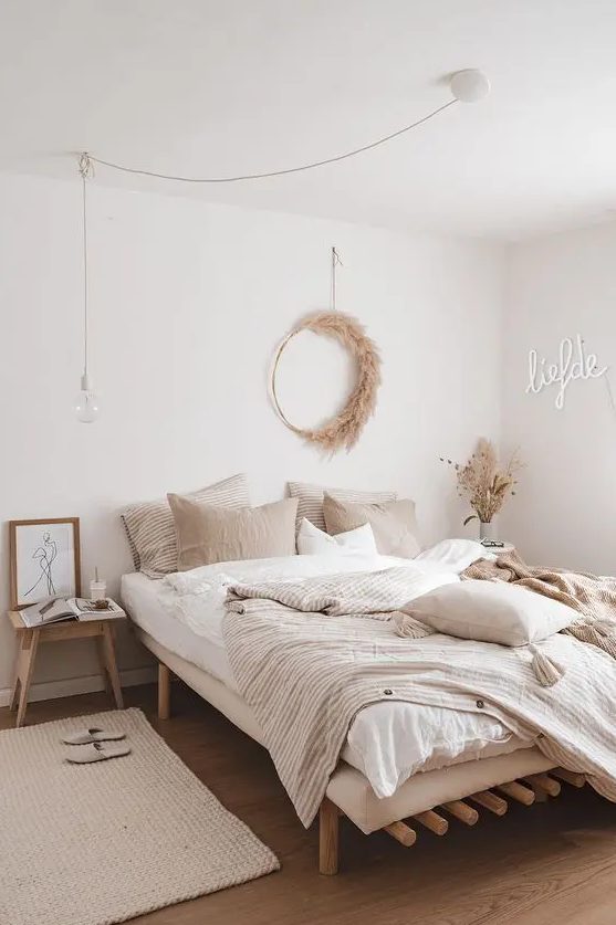 a beautiful modern boho bedroom with wooden furniture, a neon sign, a pampas grass wreath and neutral bedding