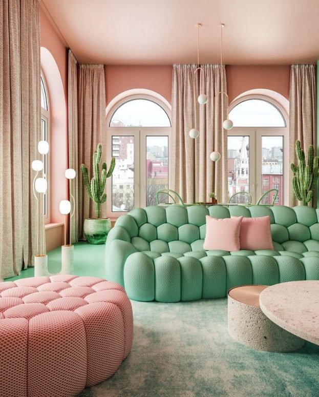 a whimsical living room with pink walls and a ceiling, neutral curtains, a pastel green sofa and a pastel pink ottoman, a green floor and planters