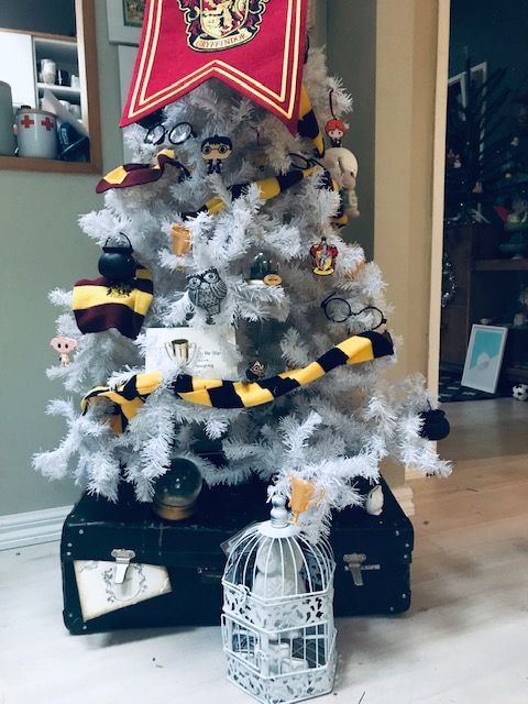 a white Christmas tree inspired by Harry Potter decorated with Griffindor scarves, owls, mini Harry Potter ornaments, cauldrons and a flag on top