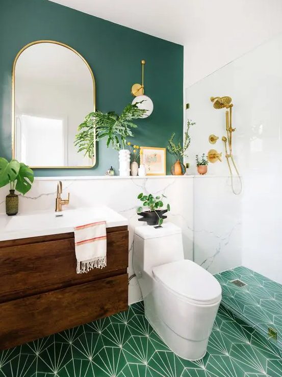 a chic modern bathroom with a green accent wall and a green mosaic tile floor, a stained vanity, an arched mirror and potted plants