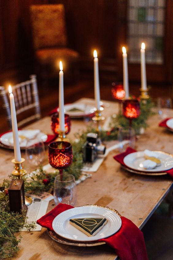 a pretty and chic Harry Potter Christmas tablescape with tall and thin candles, mini ornaments and greenery, elegant porcelain and red napkins