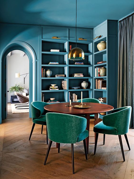 a fabulous stone blue dining space with built-in shelves and storage units, a stained dining table, teal chairs and a pendant lamp